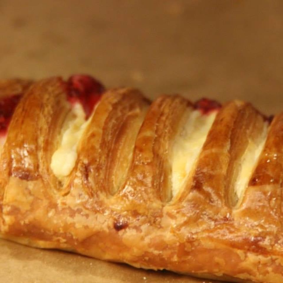 Golden braided pastry filled with creamy custard and red berry jam, resting on parchment paper.