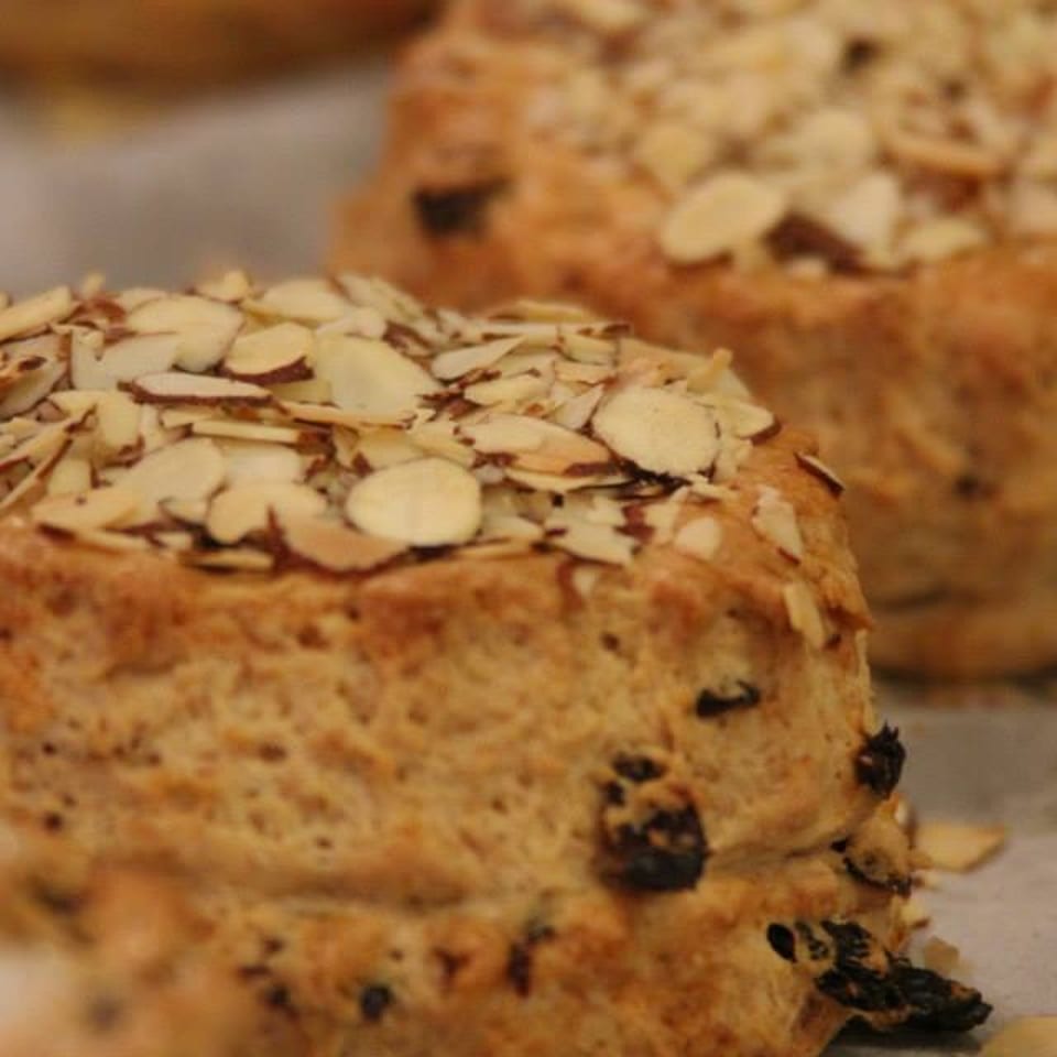 Close-up of golden baked almond-topped pastries with visible dried fruit on a baking tray.