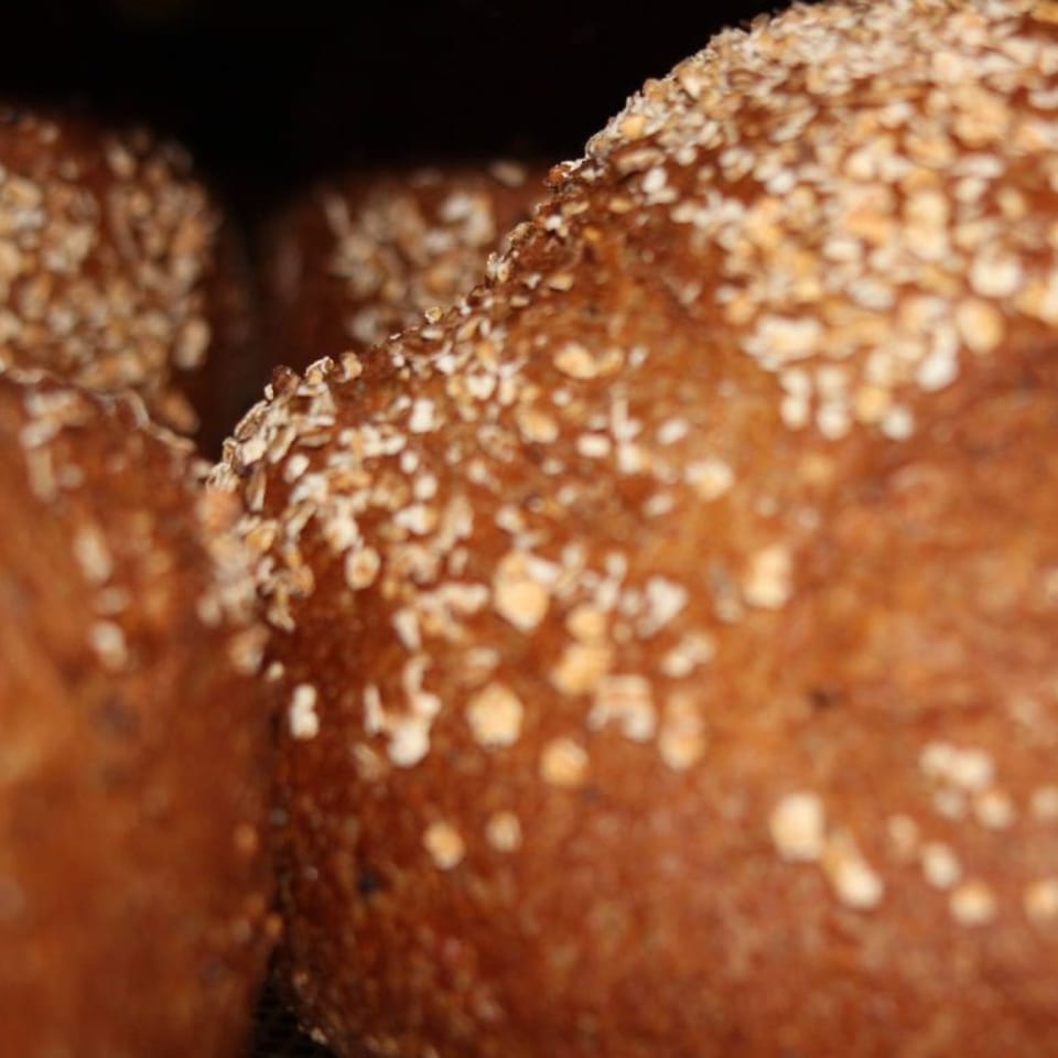 Close-up of two loaves of dark bread, sprinkled with oats, against a dark background.
